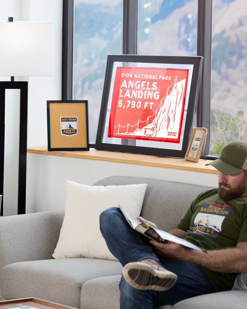 A hiker proudly showing their framed summit flag displayed in an office leaning against a wall or window.  The summit flag is made by Summit Something.