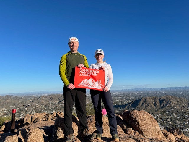 A couple proudly displays their orange Camelback Mountain summit flag on the Camelback Mountain summit- summit flag made by Summit Something also known as 5ummit 5omething