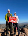 A couple proudly displays their orange Camelback Mountain summit flag on the Camelback Mountain summit- summit flag made by Summit Something also known as 5ummit 5omething