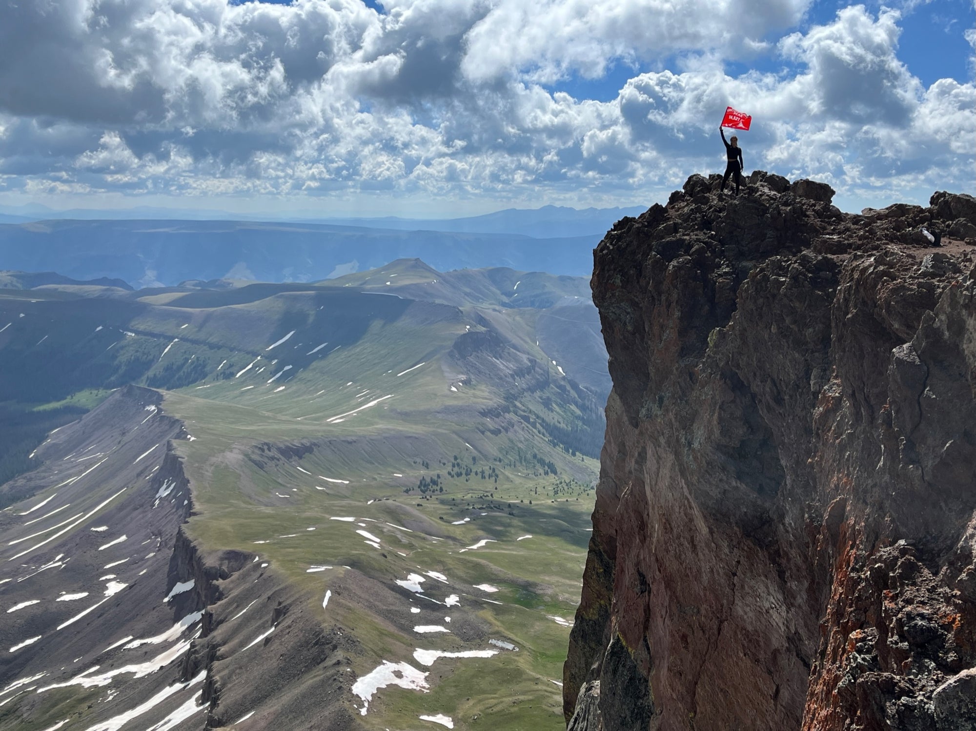 Hero Photo of the Uncompahgre Peak summit with hiker proudly holding up an orange summit flag made by Summit Something .