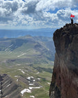 Hero Photo of the Uncompahgre Peak summit with hiker proudly holding up an orange summit flag made by Summit Something .