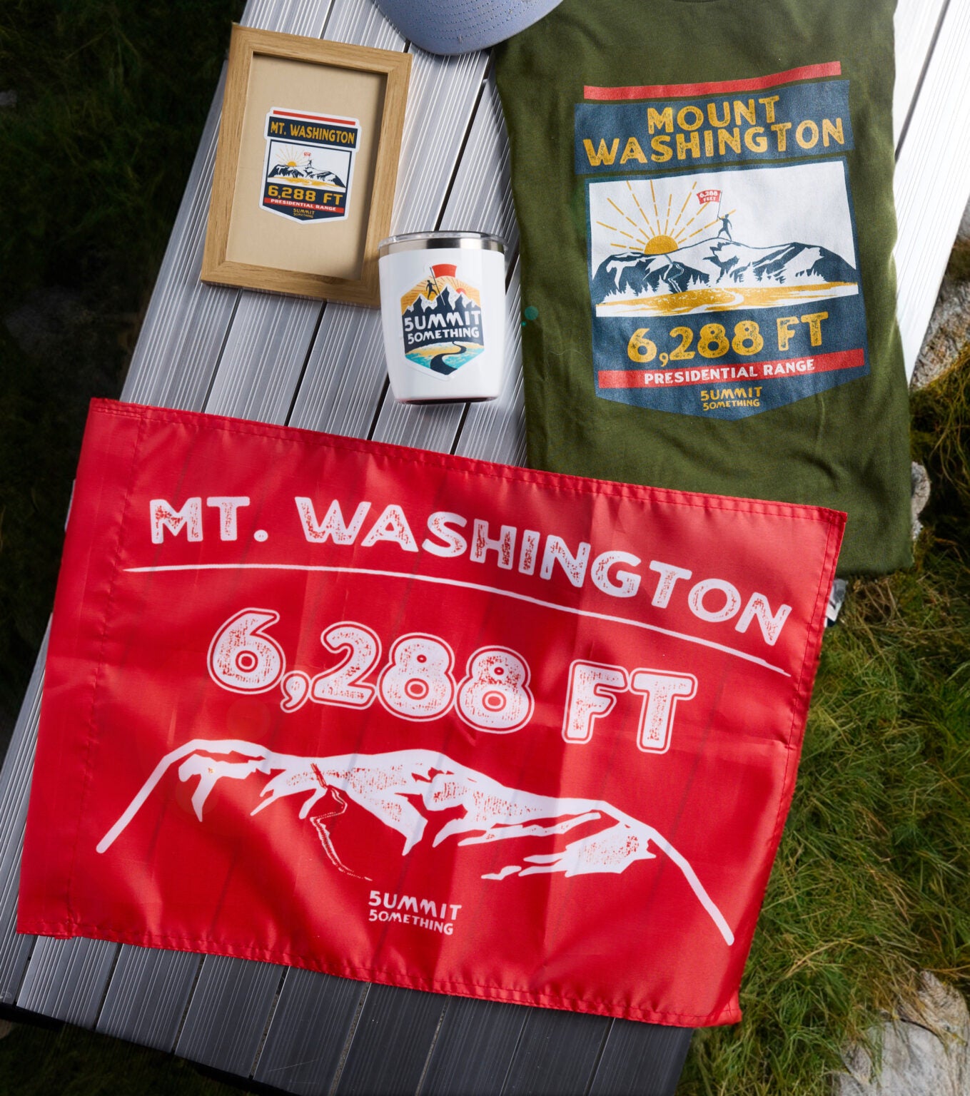 Photo displaying the Mt. Washington colletion of souvenirs including t-shirt, stickers, and orange summit flag made by Summit Something also known as 5ummit 5omething.