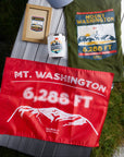 Photo displaying the Mt. Washington colletion of souvenirs including t-shirt, stickers, and orange summit flag made by Summit Something also known as 5ummit 5omething.