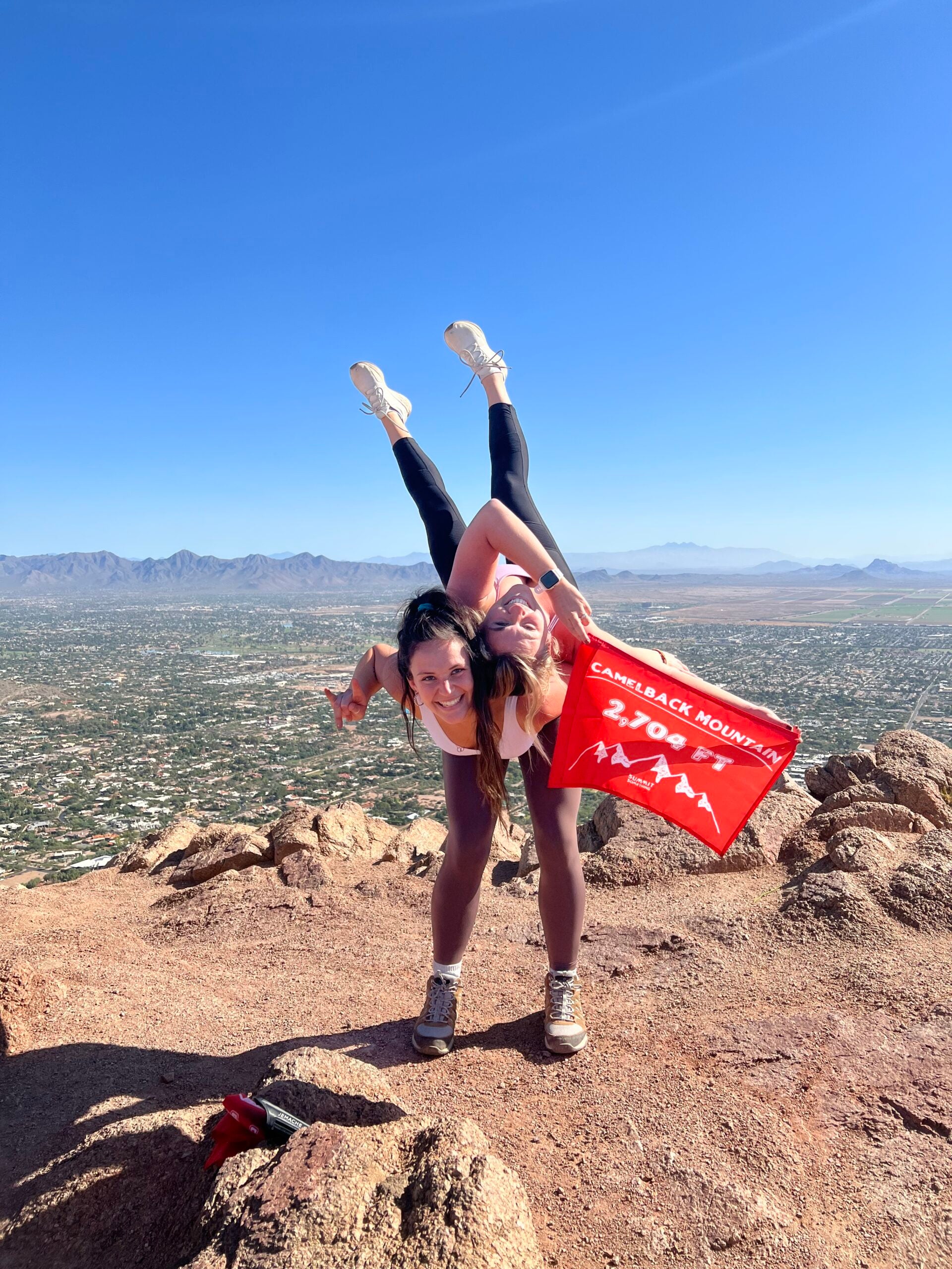 Two girls celebrating the 360-degree view on the Camelback Mountain summit with a 5ummit 5omething summit flage.