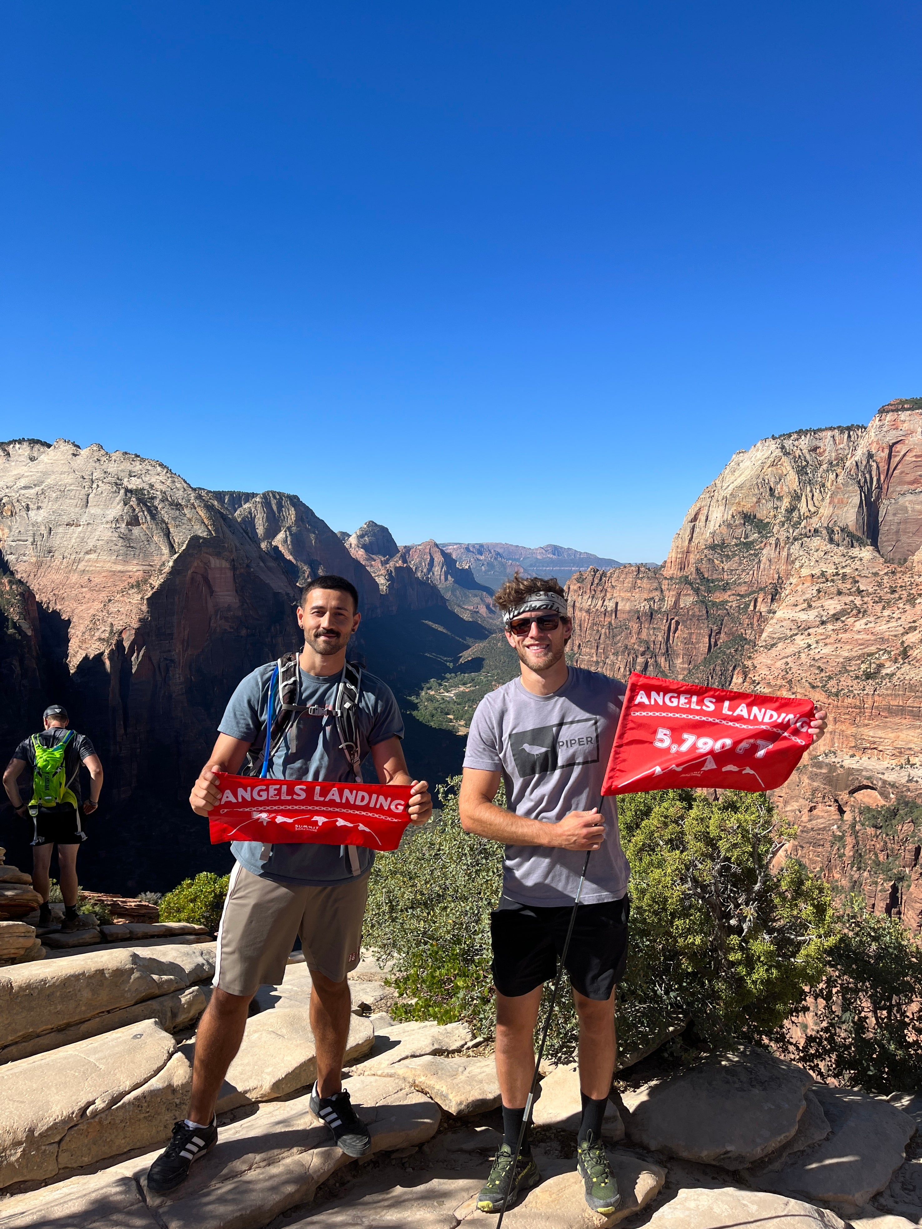 Hikers on the Angels Landing summit in Zion National Park proudly showing off their orange summit flags made by Summit Something.