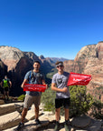 Hikers on the Angels Landing summit in Zion National Park proudly showing off their orange summit flags made by Summit Something.